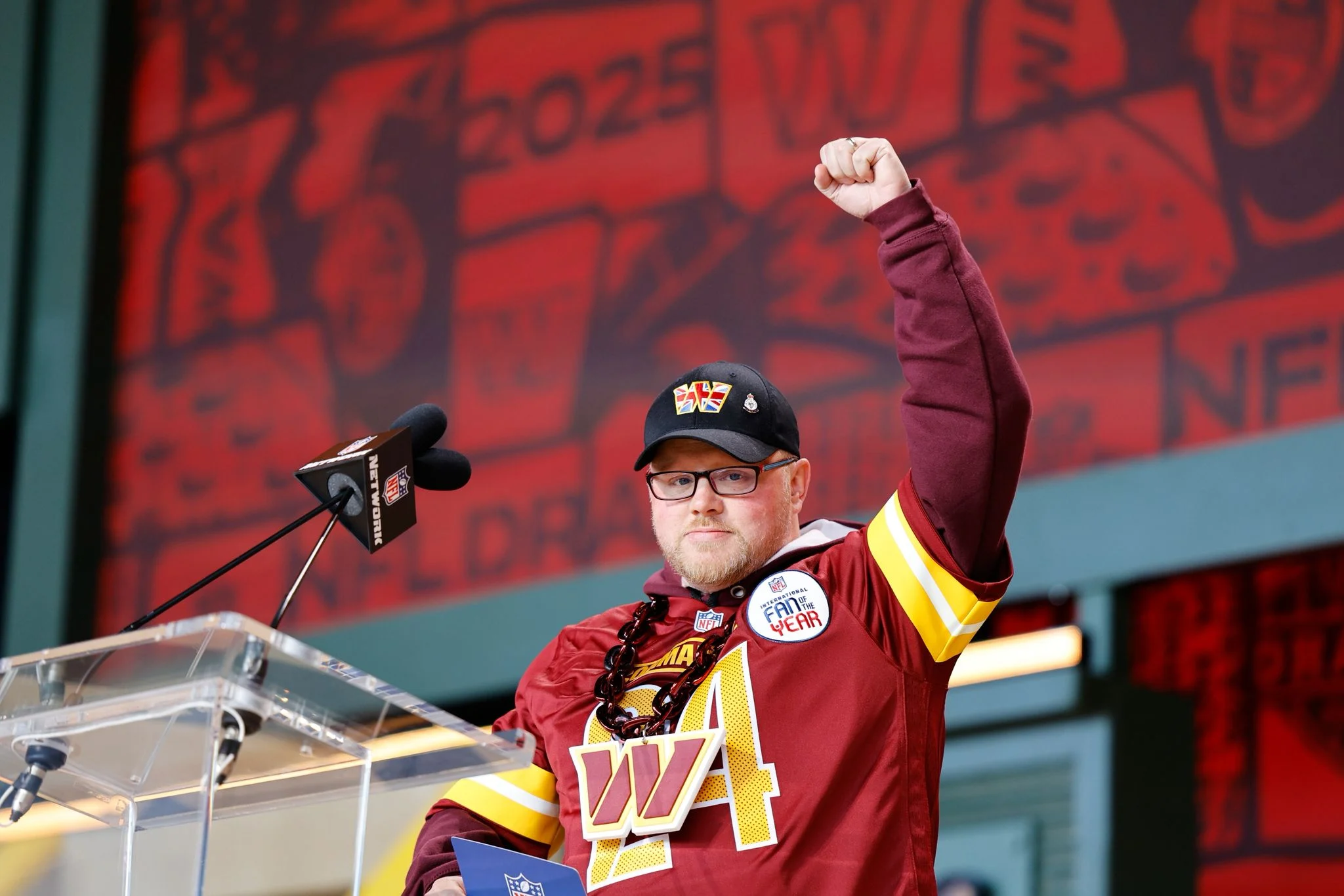 International Fan of the Year Scott Hartley at the podium of the NFL draft to make the Commanders 6th round pick, LB Kain Medrano